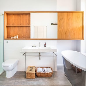 A bathroom with a white sink, a toilet, a wooden vanity with a mirror, and a bathtub. - Exceptional Renovated Period Home in Clifton (Bristol)