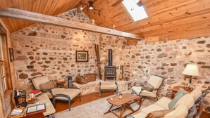 A cozy room with stone walls, wooden ceiling beams, a fireplace, and comfortable seating. - Beautifully Restored Historic Victorian (Waukesha)