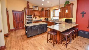 A kitchen with wooden cabinets, a central island with stools, a built-in oven, and a large window. - Beautifully Restored Historic Victorian (Waukesha)