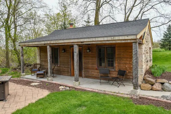 A rustic cabin with a covered porch, stone pillars, and a small outdoor seating area.