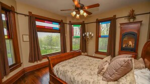 A bedroom with a wooden bed, stained glass windows, and a ceiling fan. - Beautifully Restored Historic Victorian (Waukesha)
