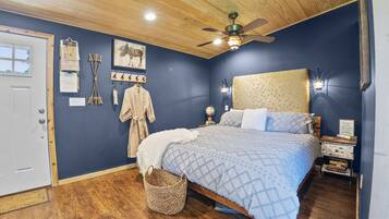 A bedroom with a bed, wooden ceiling, a ceiling fan, a nightstand, a lamp, and a wall with various items.