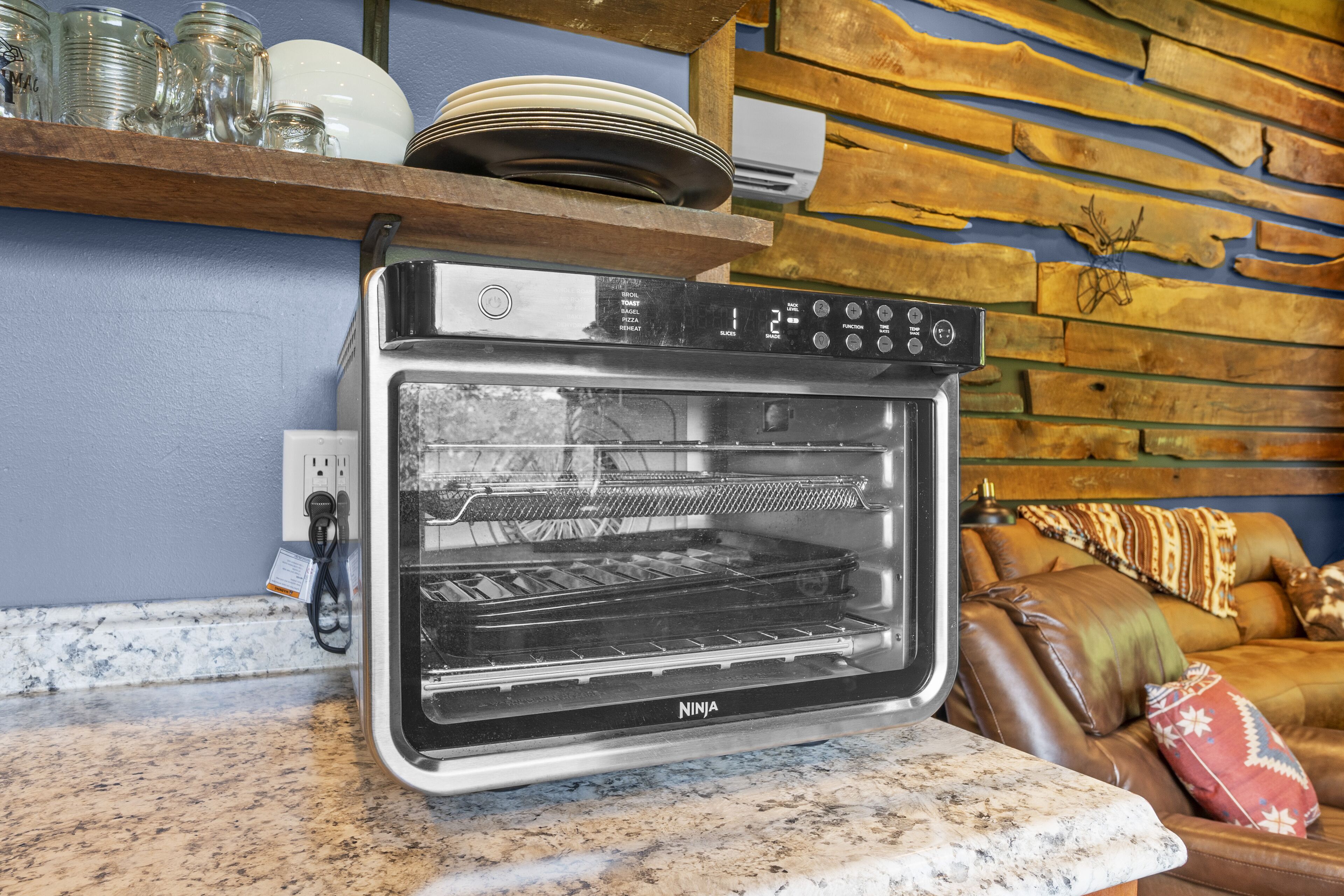 A kitchen with a built-in oven, a wooden shelf with dishes, and a stone wall.