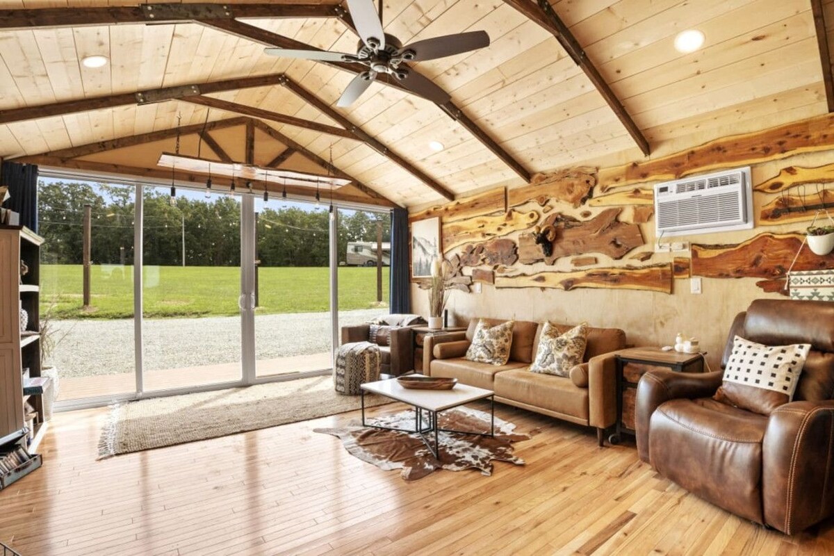 Amplia sala de estar con techo de madera, mobiliario de cuero y un gran ventanal con vistas al exterior.
