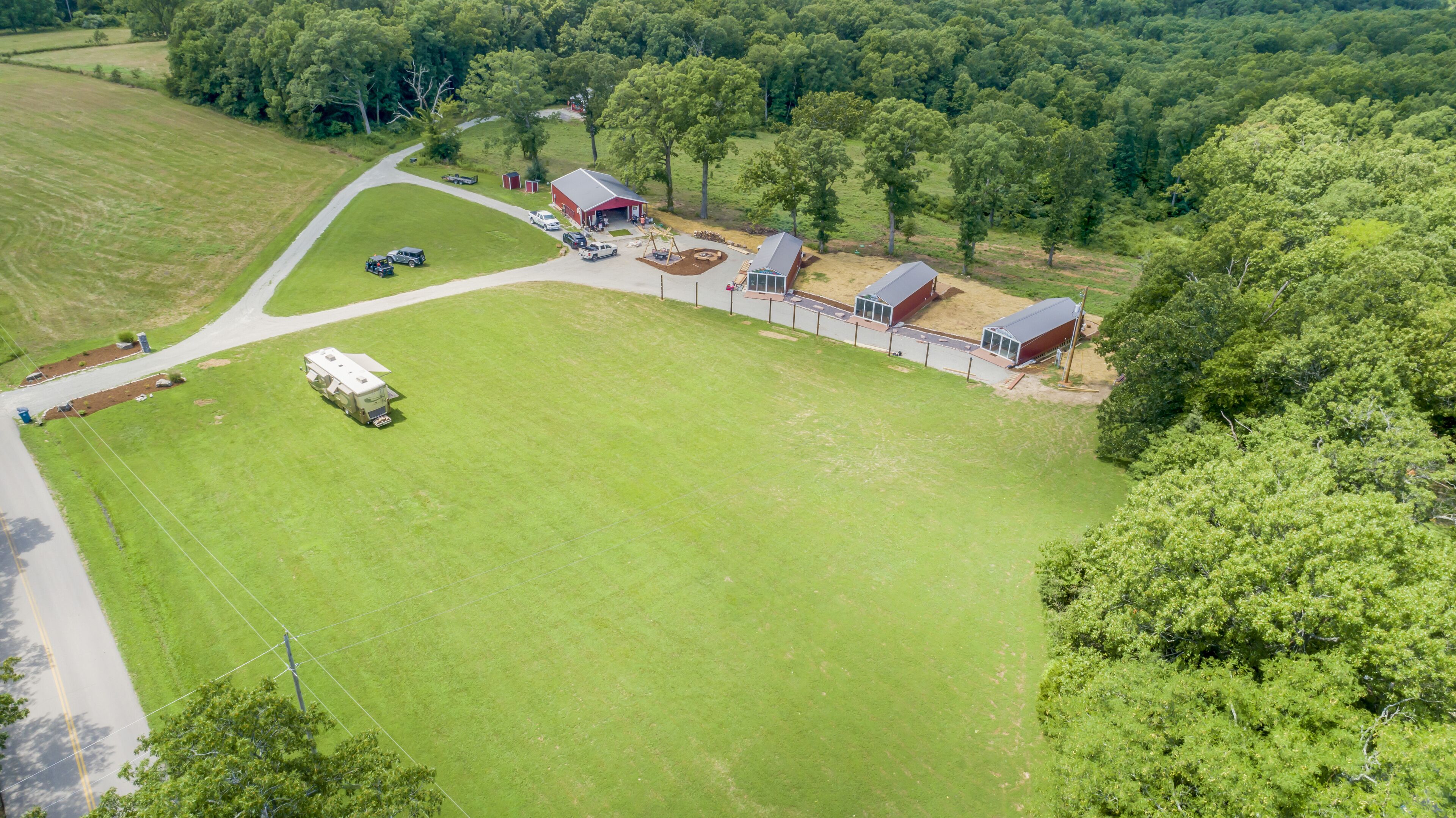 An aerial view of a property with a large green field, a red barn, and a mobile home.