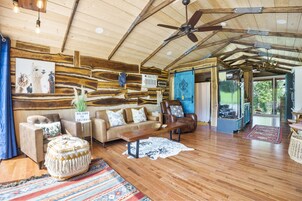 Uma sala de estar ampla com teto de madeira, ventilador de teto, sofá, mesa de centro e uma grande janela com vista para o exterior.