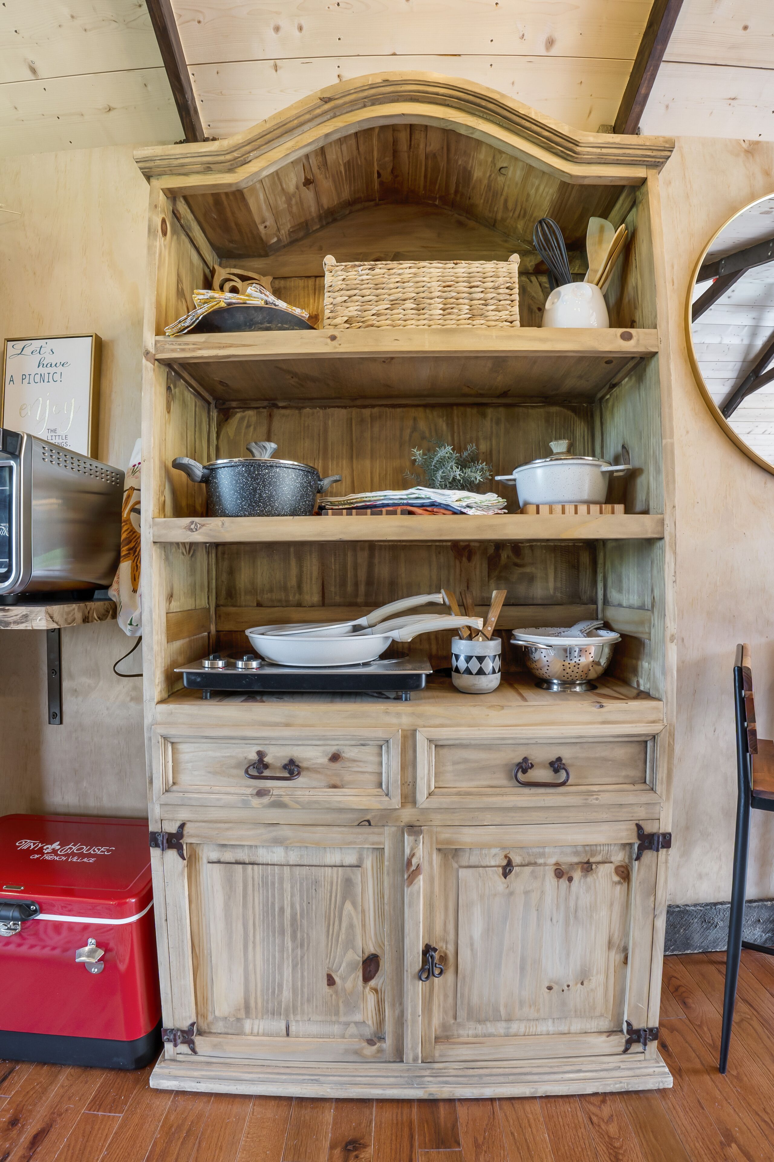 A wooden cabinet with shelves and drawers, containing kitchen utensils and cookware.
