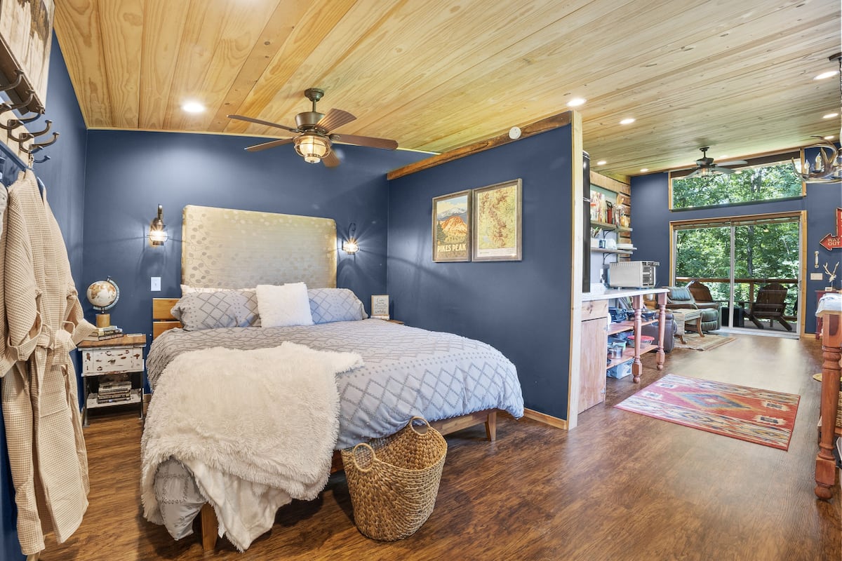 A bedroom with a large bed, wooden ceiling, and a view of the outdoors.