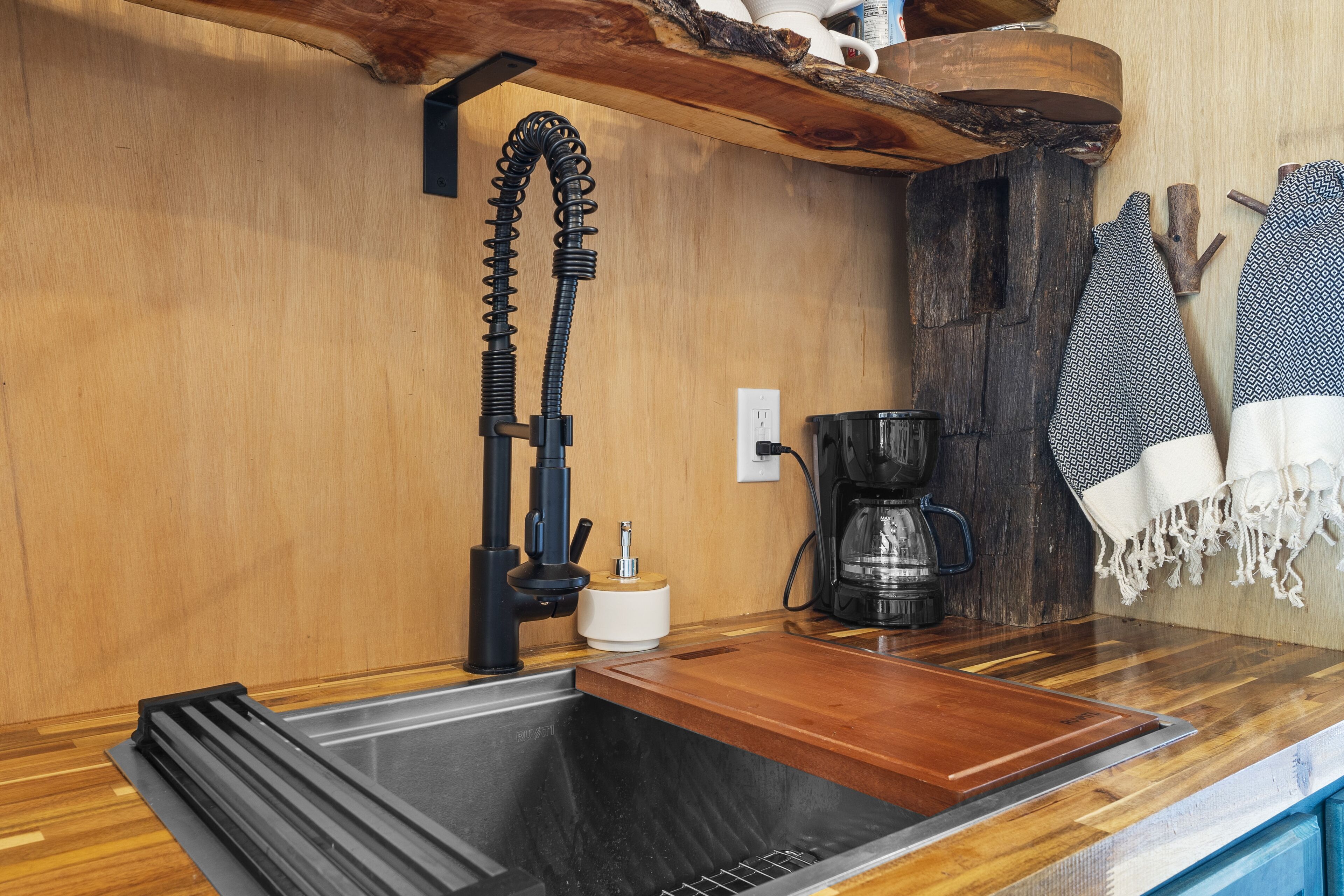A kitchen with a wooden countertop, a sink, a coffee maker, and a shelf with a kettle.