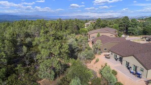 A residential area with multiple houses surrounded by dense forest, featuring a patio with outdoor furniture and a clear view of distant mountains. - Watching Wildlife: Private Oasis for 4 w/ Patio, BBQ & Parking. Step Inside! (Payson)
