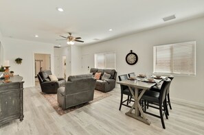 Un salon moderne avec un canapé gris, une table à manger avec des chaises et un ventilateur de plafond.