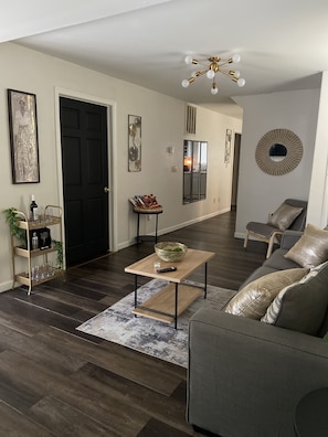 A modern living room with a dark wood floor, a grey sofa, a coffee table, and a black door.