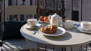 A table with a croissant, coffee cups, and a teapot on a balcony with a view of historic buildings. - Fosca Venice Rooms (Venice)