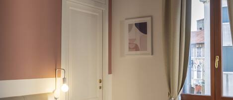 A bedroom with a bed, a nightstand, a wall-mounted lamp, a door, a window with curtains, and a ceiling fan.