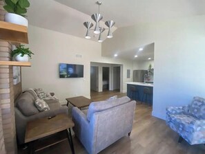 Relax in this stylish living space with a sofa, armchair, and coffee table, plus a kitchen area with a countertop and stools.