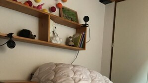 Une chambre à coucher avec un lit, une table de chevet, une étagère avec des jouets et un appareil photo.