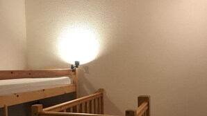 Un lit superposé avec une rambarde en bois et un luminaire fixé au mur.