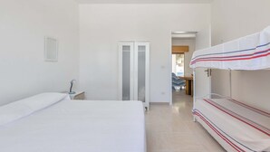 Una camera da letto con un letto, un comodino con una lampada, un armadio e un letto a castello con coperta a righe.
