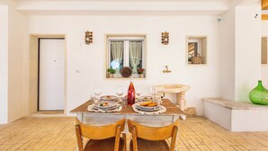 A dining area with a wooden table set for two, a window with curtains, and a small sink with a green vase.
