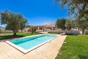 A rectangular swimming pool with a tiled deck, surrounded by a grassy lawn and trees.