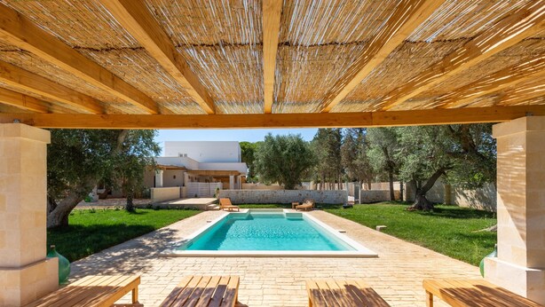 A covered outdoor swimming pool area with wooden benches and a stone pathway.