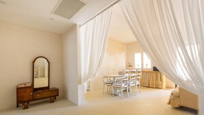 A bedroom with a canopy bed, a wooden dresser, and a dining area with chairs and a table.
