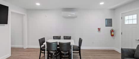 A dining area with a round table and six chairs, a fire extinguisher, and a door with a window.
