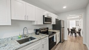 A modern kitchen with white cabinets, a stainless steel microwave, a refrigerator, a gas stove, and a sink with a faucet. - Sea La Vie Ocean City, steps away from the Beach & Boardwalk (Ocean City)