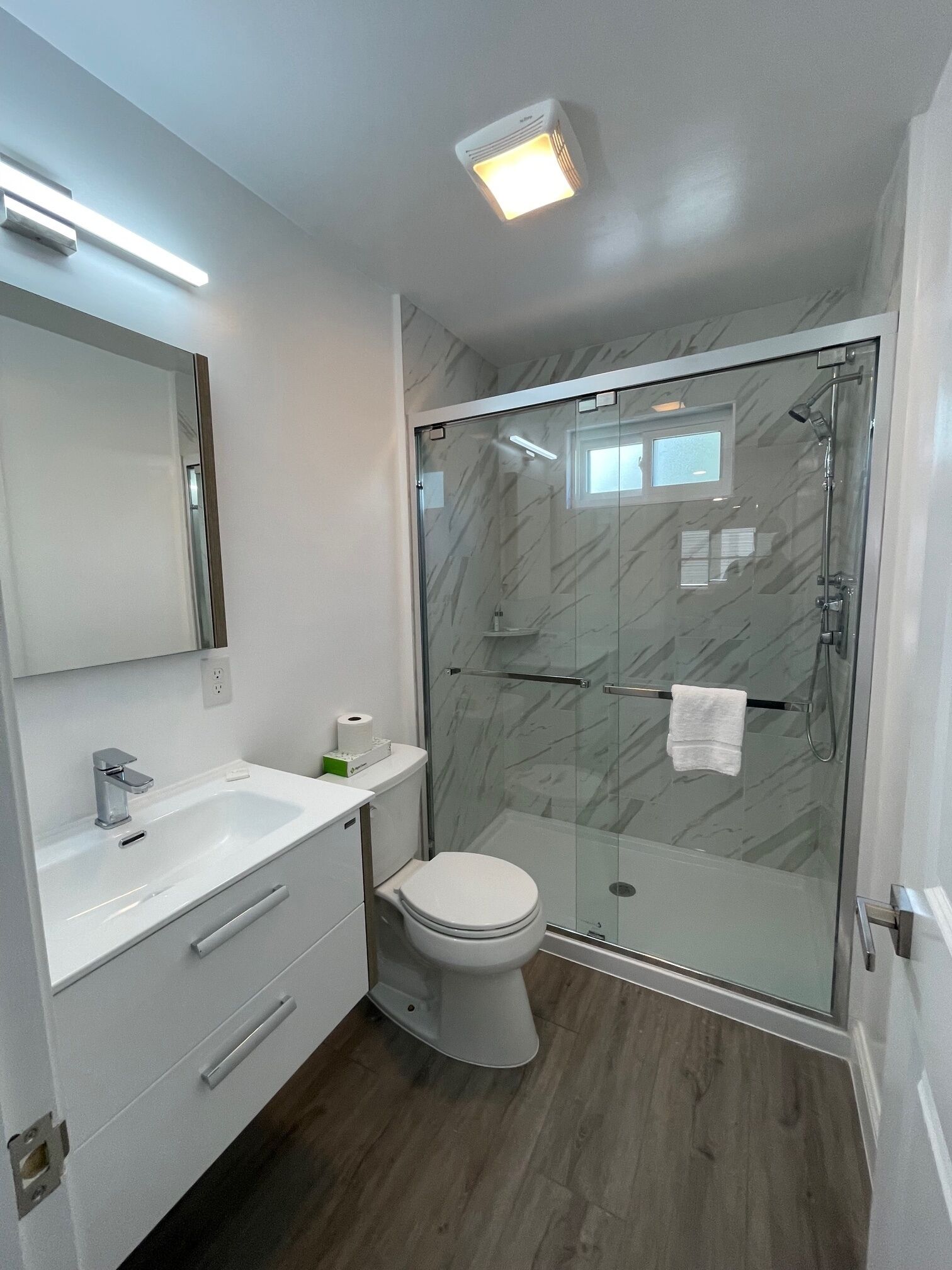 A modern bathroom with a glass-enclosed shower, a white toilet, a vanity with a mirror, and a light fixture on the ceiling.