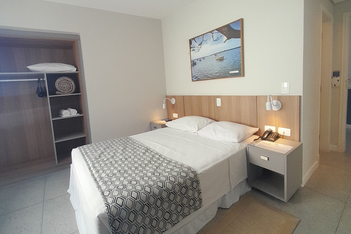 A neatly arranged bedroom with a bed, bedside tables, a nightstand, a ceiling fan, a painting, and a wardrobe.