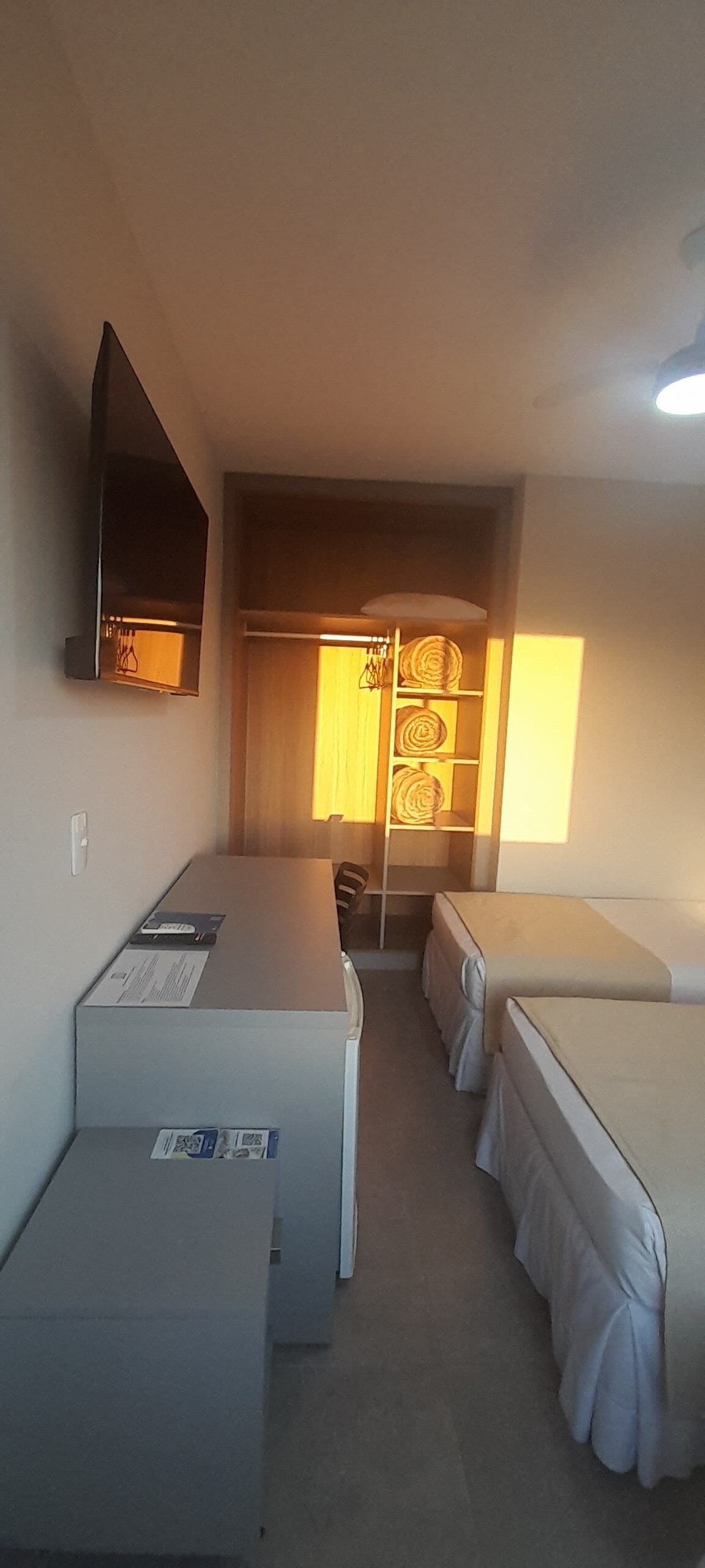 A compact hotel room with a single bed, a small desk, a chair, and a wardrobe.