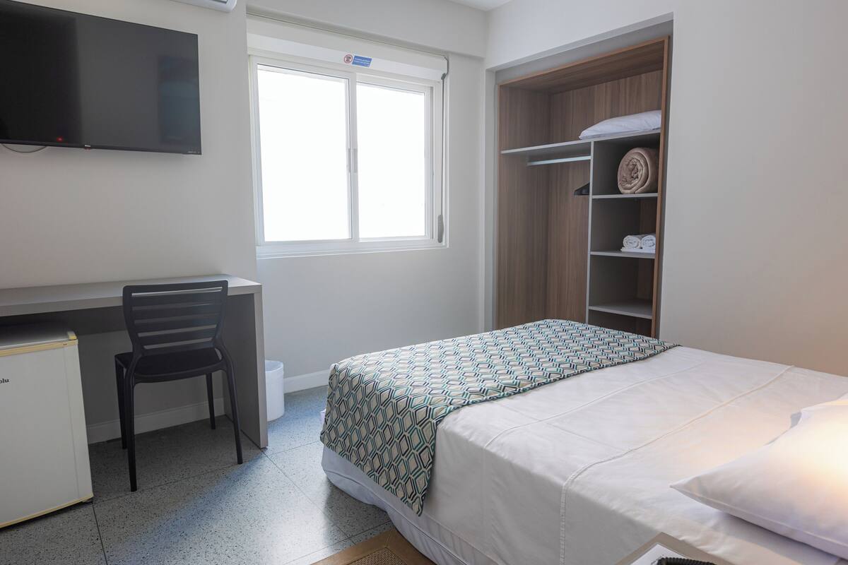 A bedroom with a bed, a desk, a chair, a wardrobe, and a television.