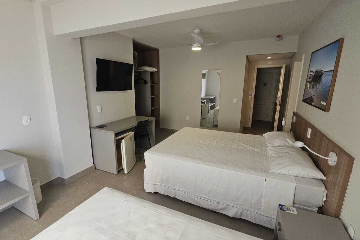 A hotel room with a bed, a desk, a chair, a wardrobe, a mirror, and a ceiling fan.