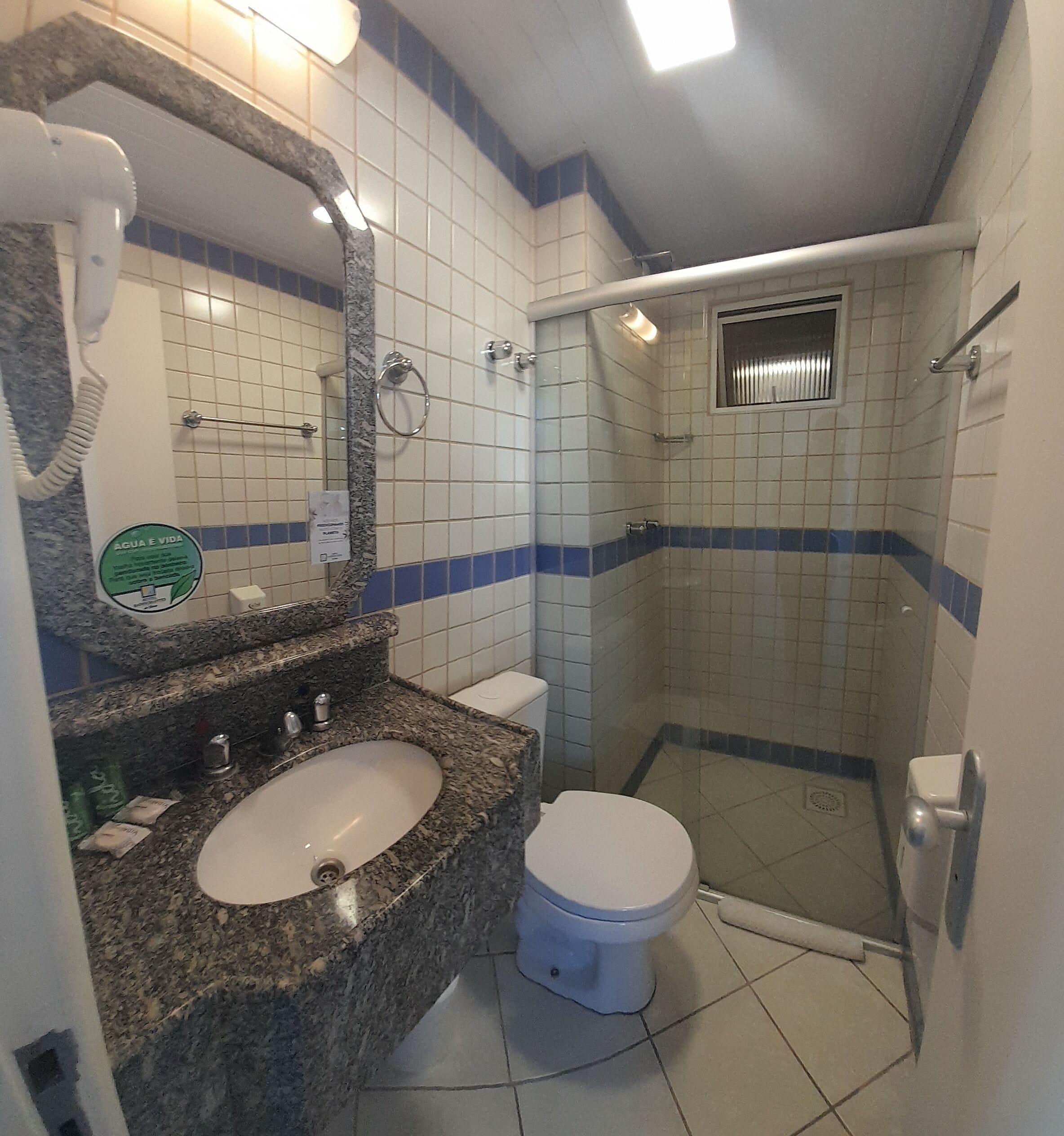 Casa de banho com lavatório de granito, sanita branca e cabine de duche com parede de vidro.