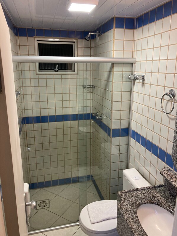 A bathroom with a glass-enclosed shower, a toilet, and a sink with a granite countertop.
