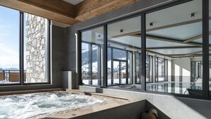 A spa area with a hot tub, stone wall, and large windows offering a view of a snowy landscape. - Wifi, fitness, swimming pool, sauna, hammam, balcony, tv, ski locker, 75m², Le Grand Bornand (Le Grand-Bornand)