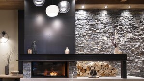 A modern living room with a stone fireplace, a black fireplace surround, and a round table with magazines. - Wifi, fitness, swimming pool, sauna, hammam, balcony, tv, ski locker, 75m², Le Grand Bornand (Le Grand-Bornand)