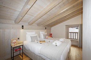 A cozy bedroom with a wooden ceiling, a bed with white linens, a small table with a board game, and a window with a view of a snowy landscape. - Wifi, fitness, swimming pool, sauna, hammam, balcony, tv, ski locker, 75m², Le Grand Bornand (Le Grand-Bornand)
