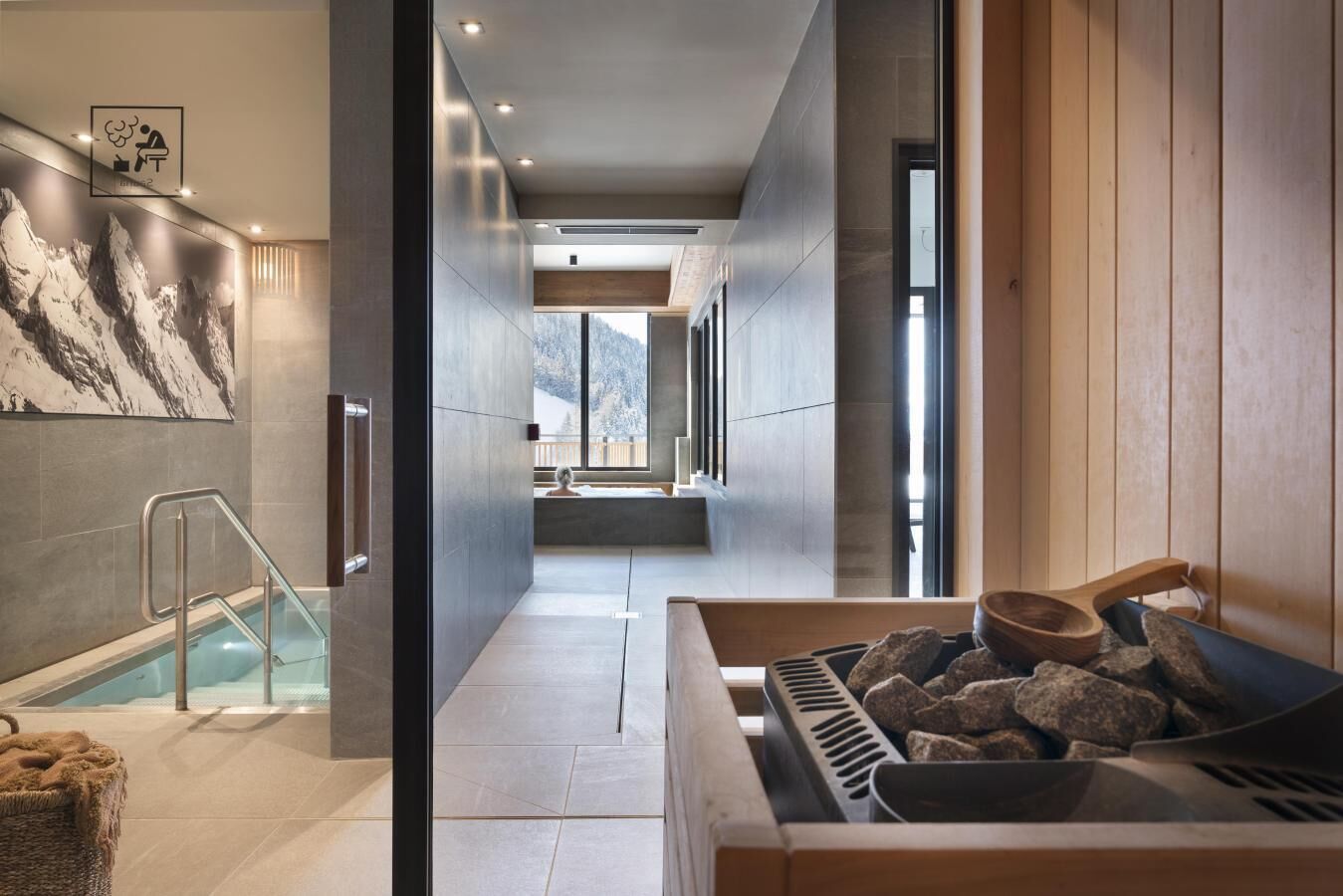 A modern spa area with a stone wall, a wooden sauna, and a glass-enclosed pool.