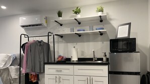 A modern kitchen with white cabinets, a stainless steel refrigerator, a microwave, and a sink. There are potted plants on a shelf above the counter. - Containing Luxury in Jensen Beach-Sandollar (Jensen Beach)