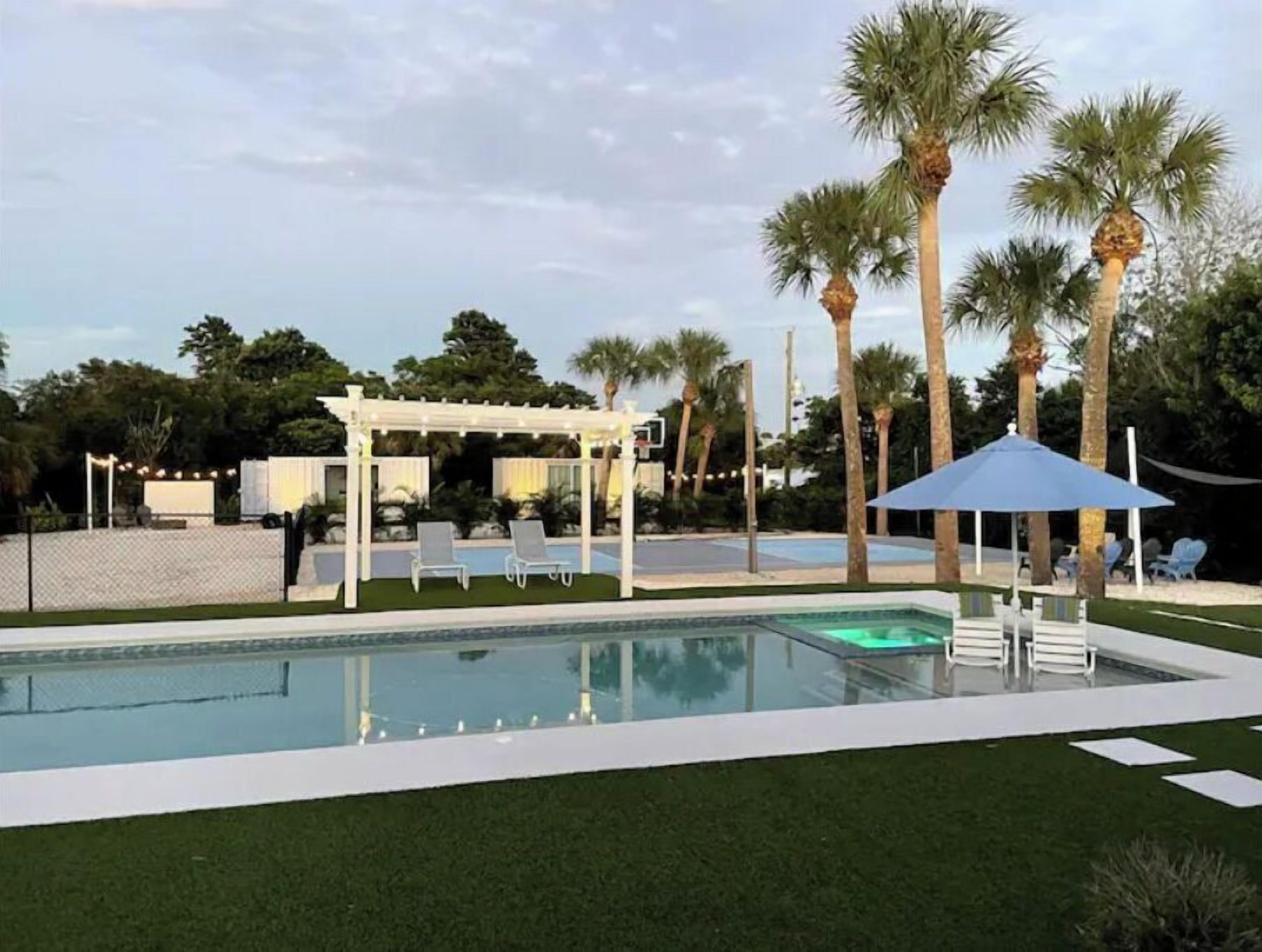 A swimming pool with a white deck, palm trees, and a covered seating area.