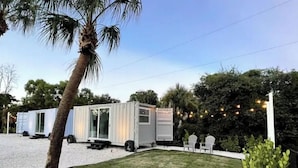 A white mobile home with a sliding door and a small porch area, surrounded by a well-maintained lawn and palm trees. - Containing Luxury in Jensen Beach-Sandollar (Jensen Beach)