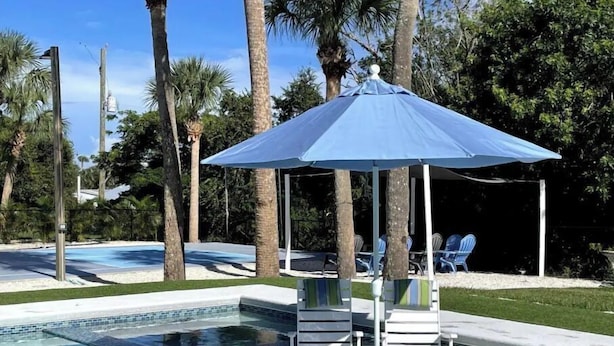A swimming pool with a blue umbrella and lounge chairs. - Containing Luxury in Jensen Beach-Sandollar (Jensen Beach)