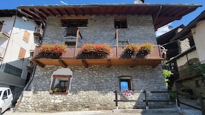 A stone building with a balcony adorned with flower boxes and a small window with a blue door. - Luciana house (Saint Christophe)