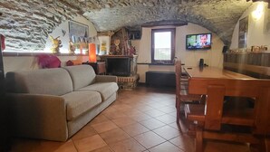 A cozy living room with a stone ceiling, a fireplace, a television, and a dining area with wooden furniture. - Luciana house (Saint Christophe)