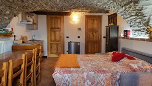 A rustic room with a wooden bed, a small kitchenette, and a stone ceiling. - Luciana house (Saint Christophe)