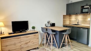 Une cuisine moderne avec un plan de travail en bois, un four à micro-ondes encastré et un évier. On y trouve deux tabourets de bar et une petite plante en pot sur le plan de travail.