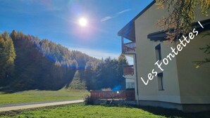 Un bâtiment moderne doté d’un balcon, entouré d’une zone herbeuse et d’une colline boisée.
