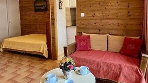 A cozy room with a wooden wall, a bed with a yellow bedspread, a red sofa with matching cushions, and a small table with a vase of flowers and cups. - 100m from ski slopes, 5th floor, tv, 30m², Vars (Vars)