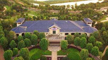 A large building with a blue roof, surrounded by trees and a lake in the background.